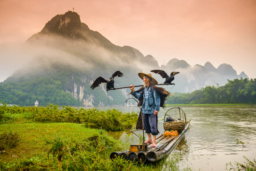 Pescador de cormoran sobre una lancha en yangshou y montañas de fondo